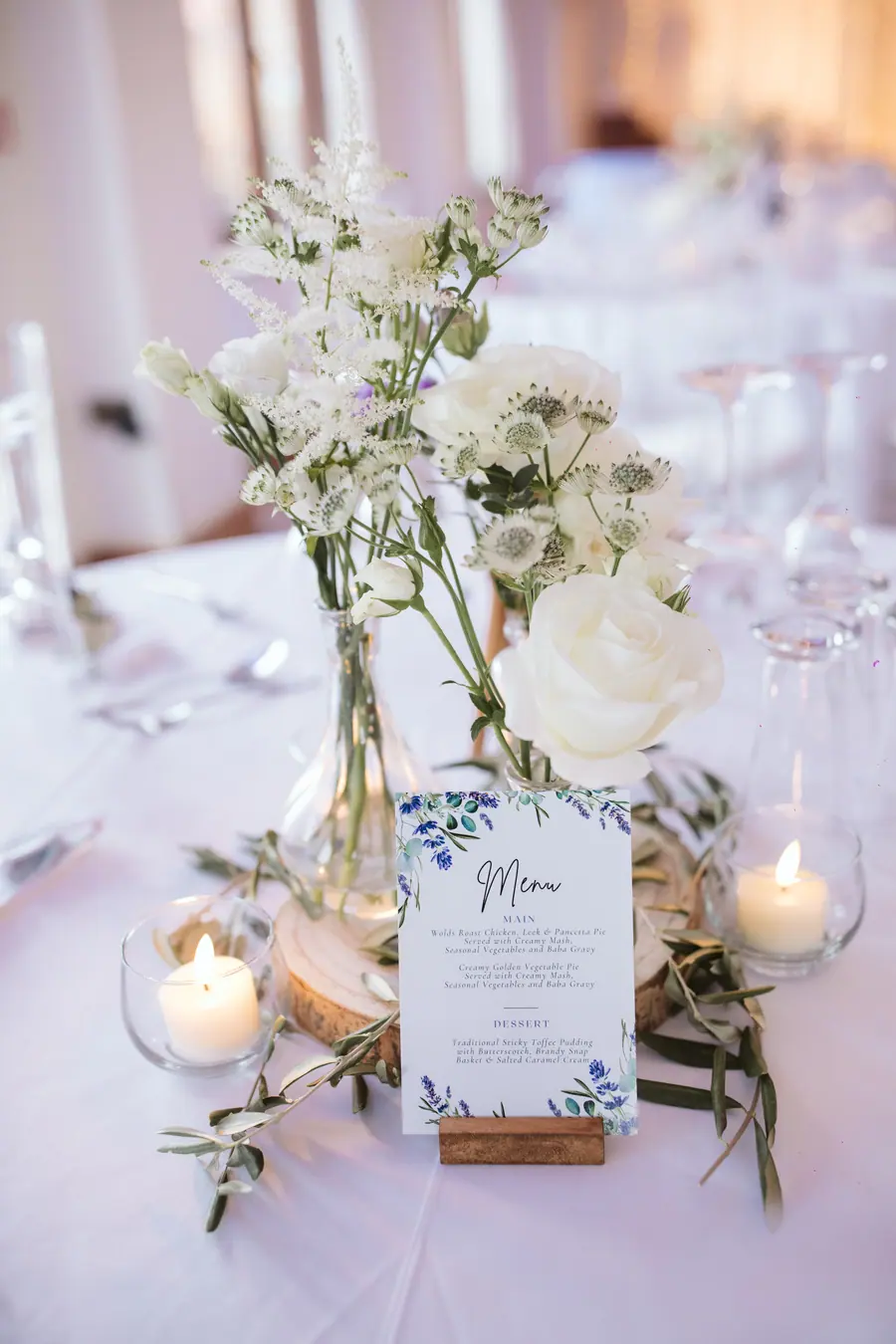 Printed wedding menu beneath white flowers, candles and delicate greenery