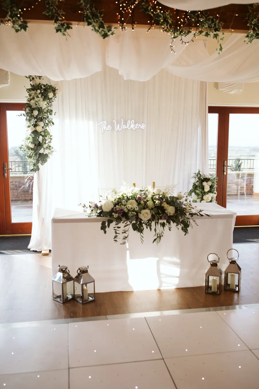 Top table beneath pale drapes with flowers and lanterns across the front