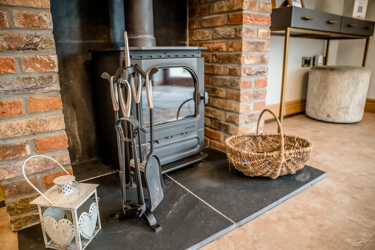 Log burner, brick fireplace and wicker basket inside Bateman Byre
