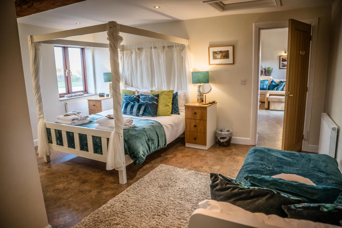 A four-poster bed with teal bedding and a sofa in a Thief Hall cottage