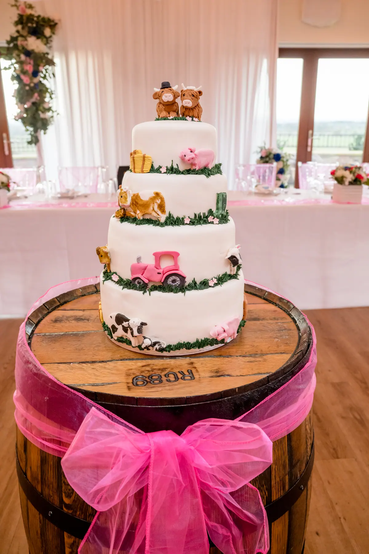A tiered wedding cake on a barrel tied with a bright pink bow