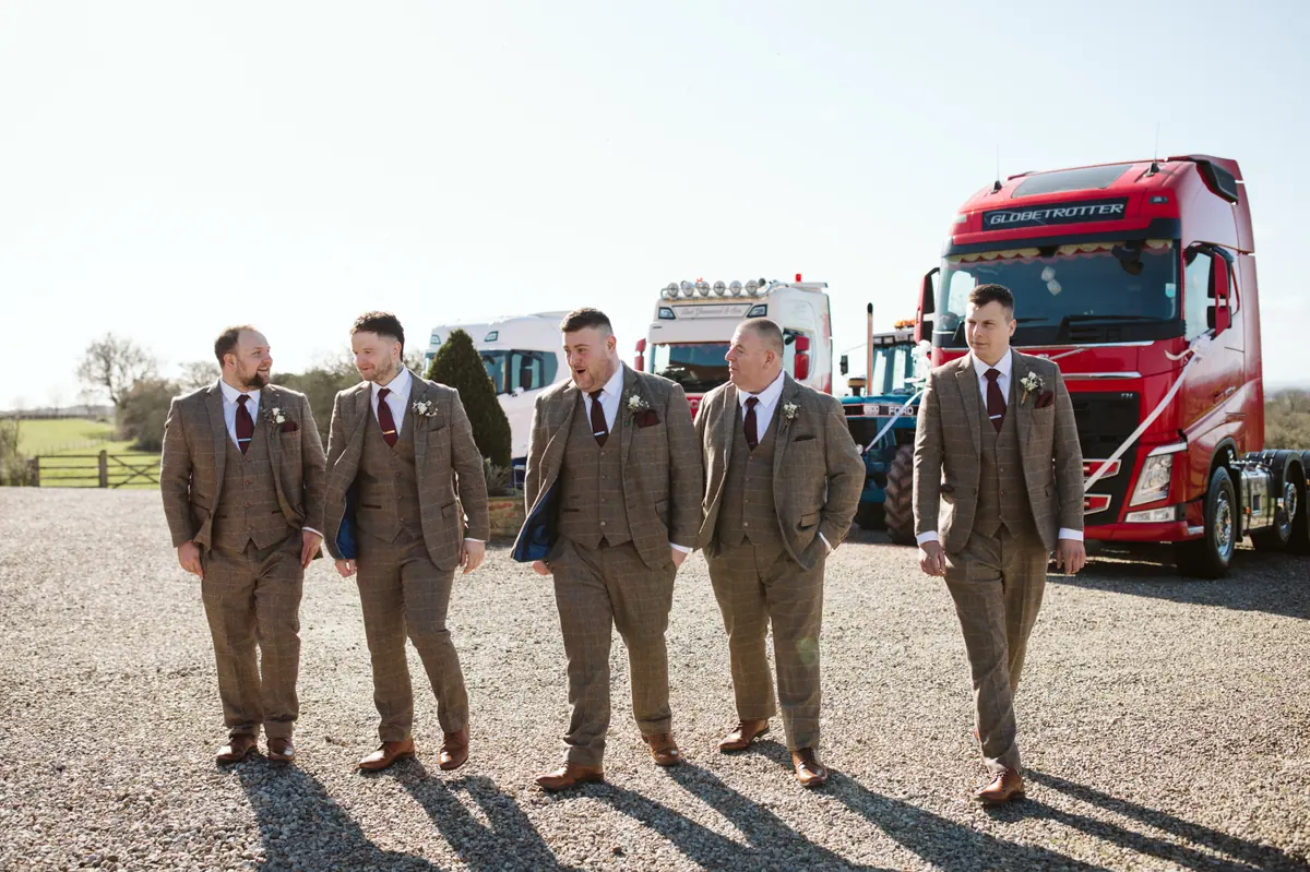 Wedding party in matching suits with decorated lorries behind them