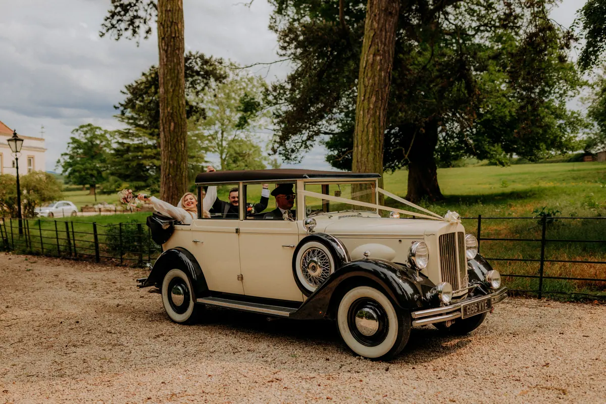 A vintage cream wedding car beneath the trees at Thief Hall