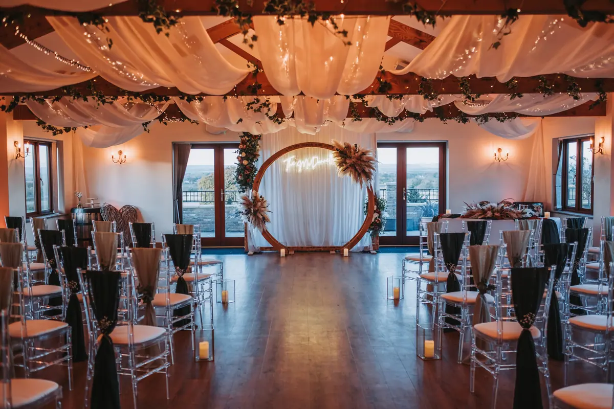 Big Hall ceremony aisle beneath ceiling drapes and fairy lights, leading to a floral arch
