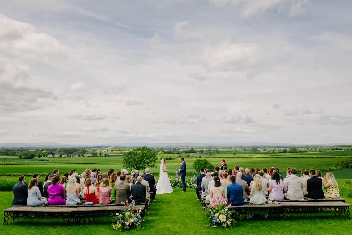 Guests seated on outdoor benches for a ceremony overlooking the North Yorkshire fields