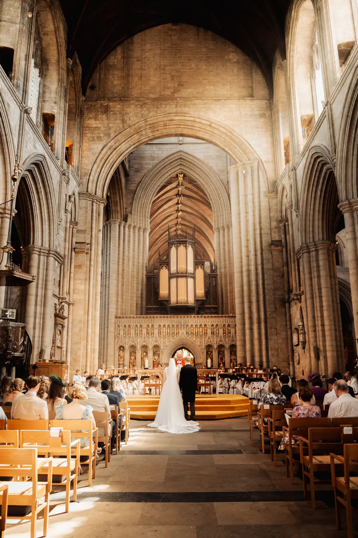 A couple exchanging vows before their guests beneath the stone arches of a church