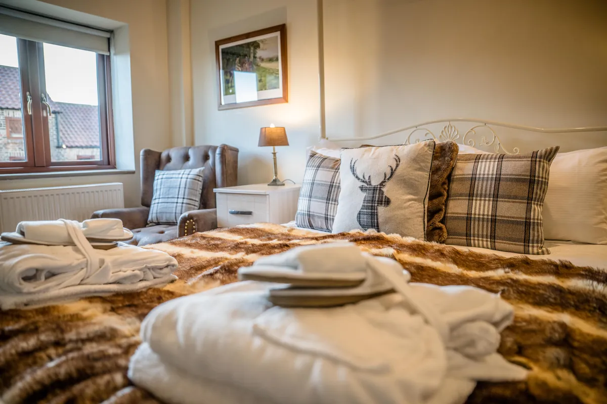 The bed in Turpin Cottage with a stag cushion, folded towels and a bedside lamp