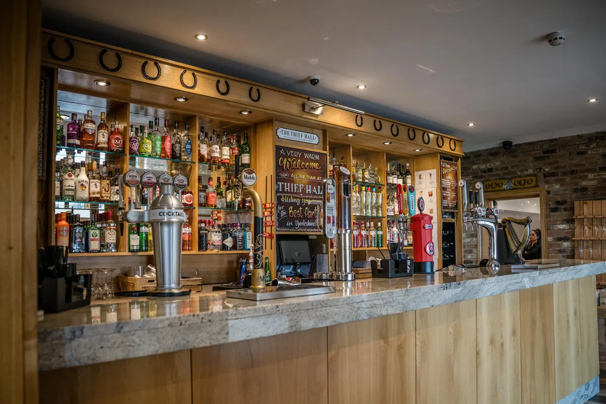 A row of iron horseshoes fixed points-up above the stocked Thief Hall bar
