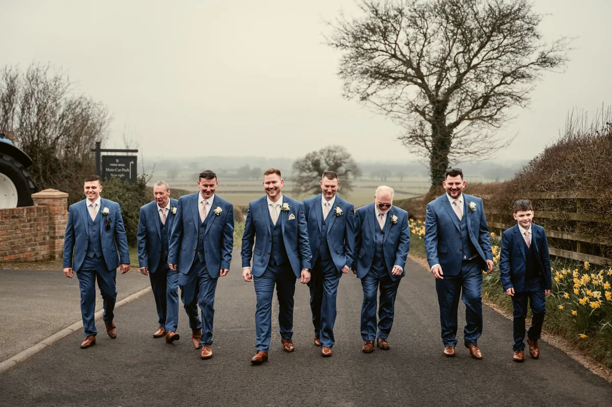 A groom and his wedding party walking together beside the barns
