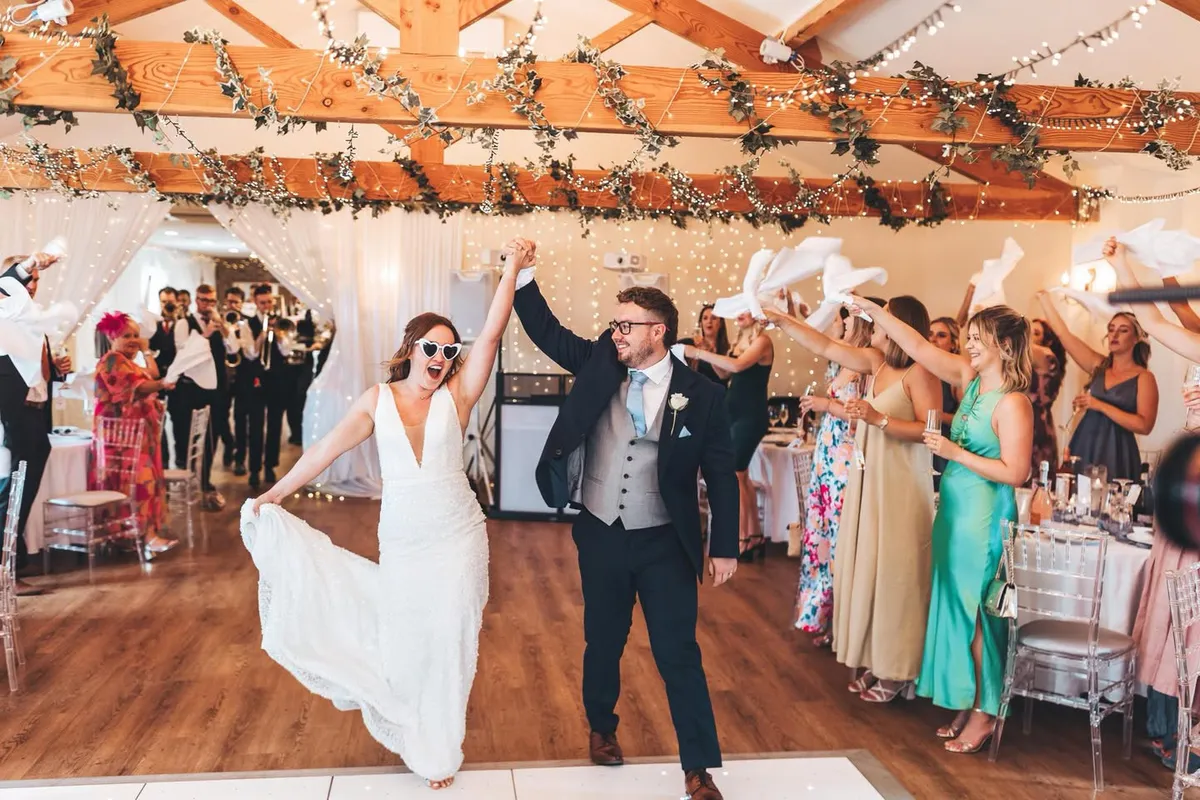 Newlyweds entering the Hall with their hands raised as guests wave napkins in celebration