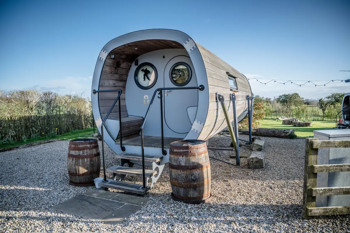 A curved timber pod with round windows, metal edging and barrel tables