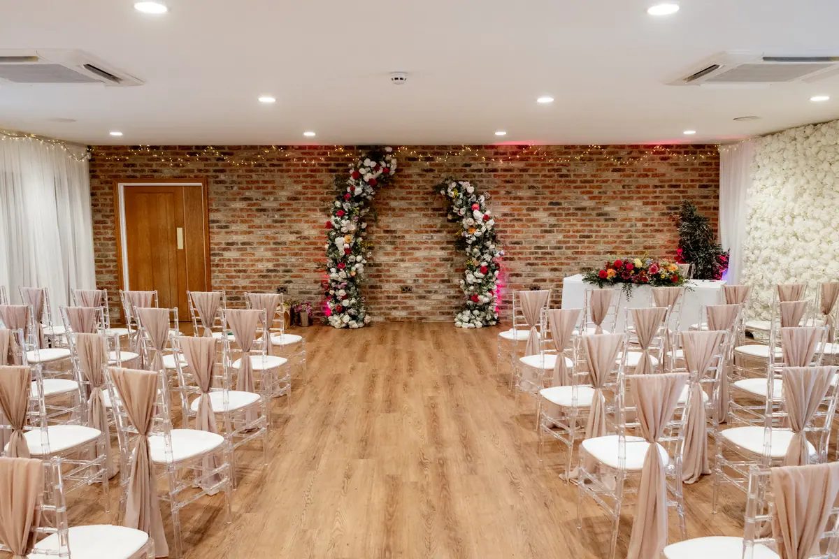 Clear ceremony chairs tied with beige fabric facing two floral columns
